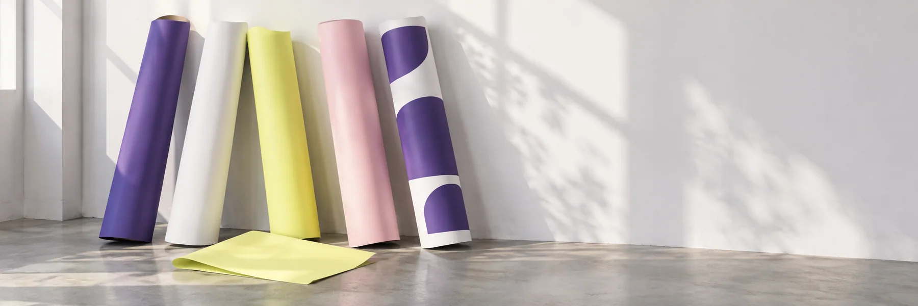Cinq rouleaux d’affiches violettes, jaunes, roses et blanches contre un mur clair.